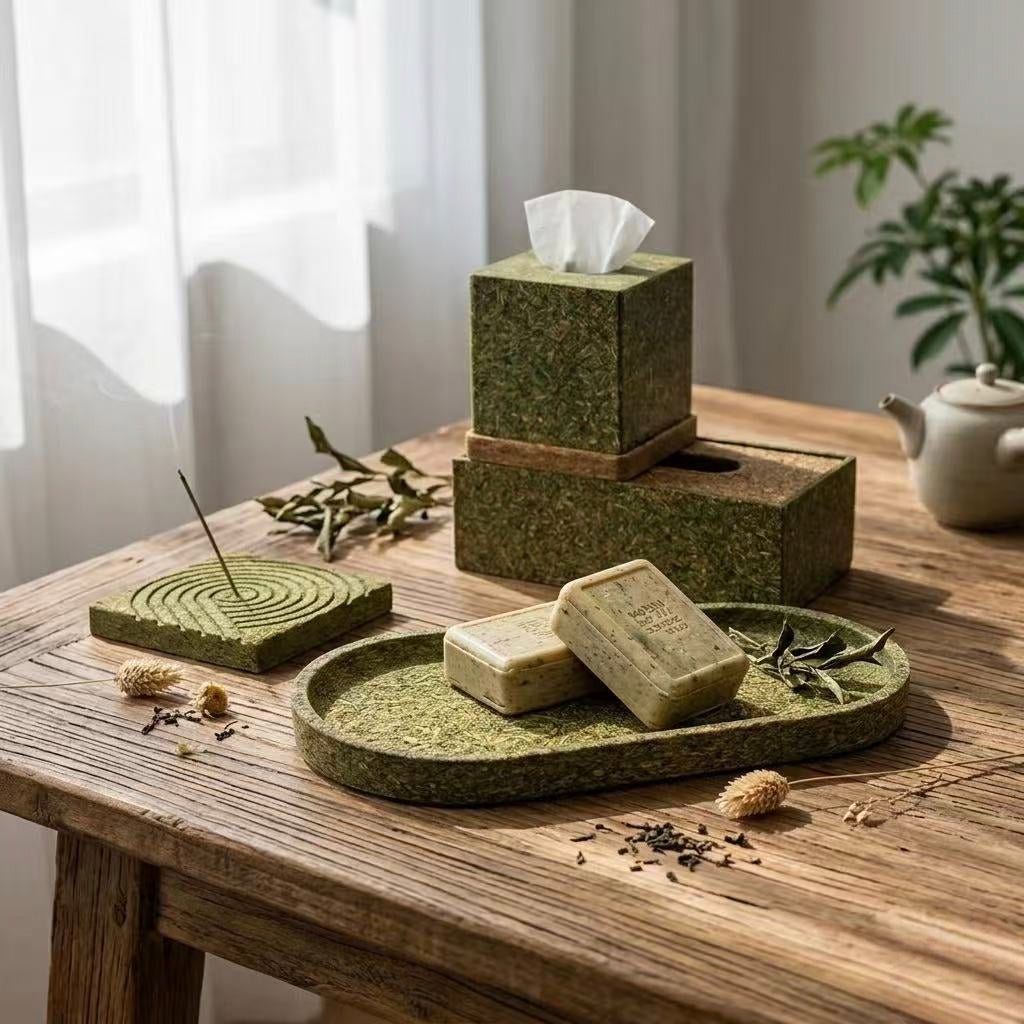 Eco-friendly home decor collection made from recycled tea waste, featuring a textured oval tray, incense holder, and tissue box on a wooden desk.