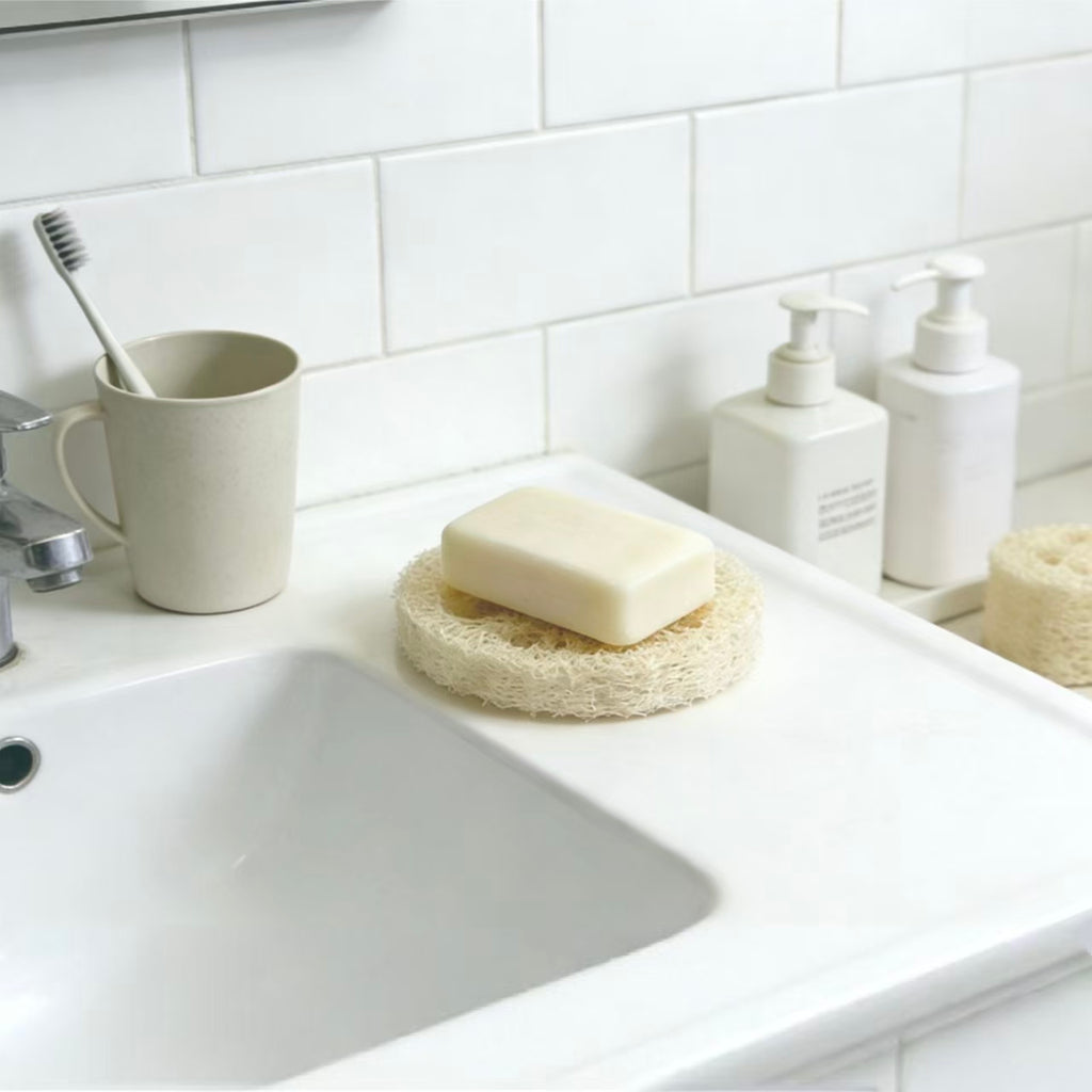 Natural loofah soap saver pad on bathroom counter, plastic-free plant fiber soap rest for handmade soap