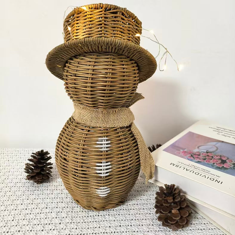  An artisanal handwoven natural rattan snowman holiday decoration illuminated with warm fairy lights on a cozy white tabletop layout with pinecones.