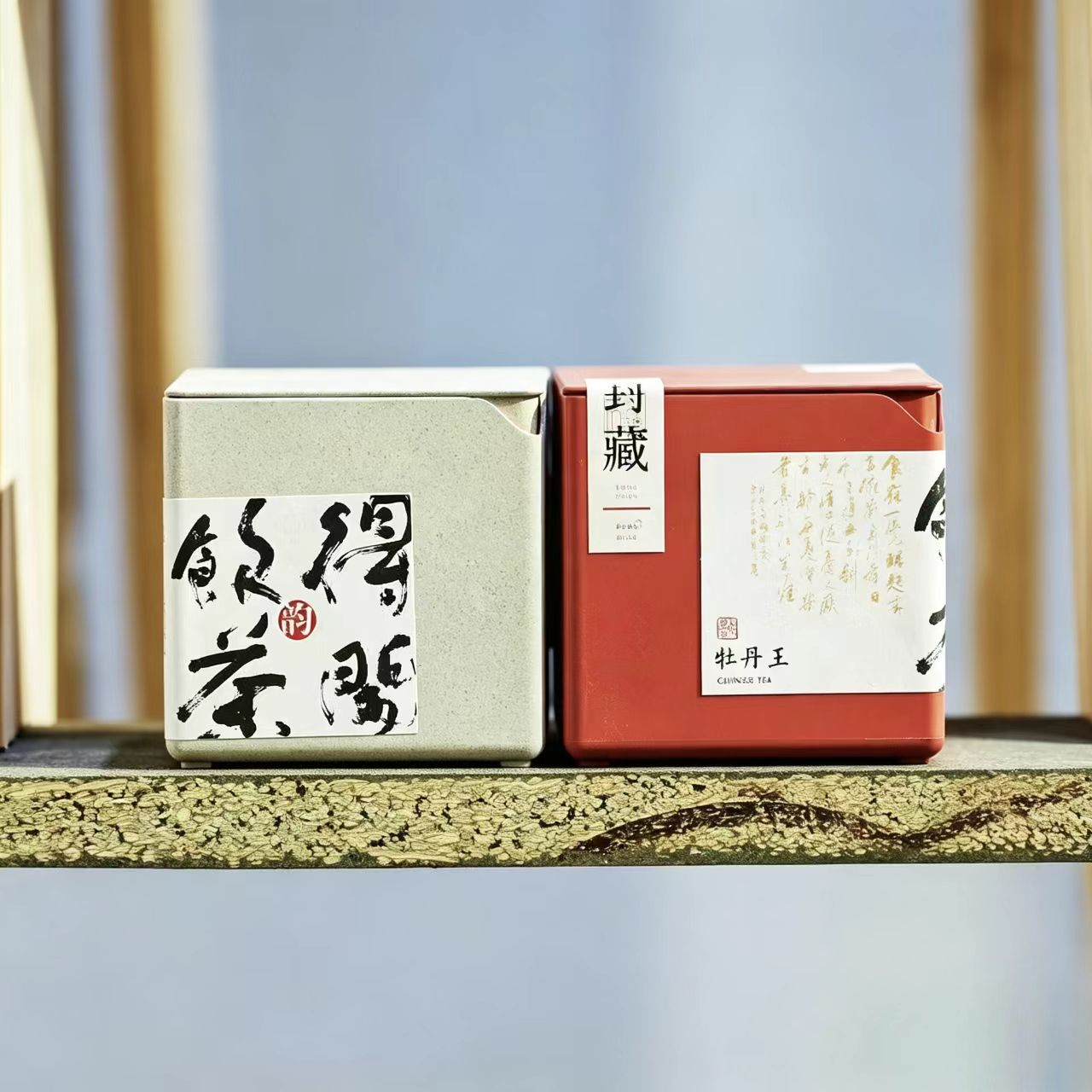  Two premium minimalist tea packaging boxes—one sand gray and one imperial red—made from biodegradable tea fiber composite material, featuring elegant Chinese calligraphy labels.