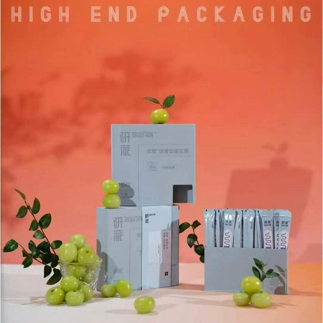 A functional gray outer packaging box made from tea-fiber bio-composite material, featuring a lower opening designed for dispensing supplement stick packs, displayed against a vibrant orange background.