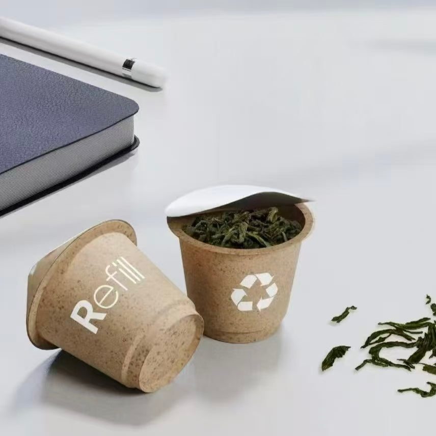 Biodegradable refillable single-cup tea pods containing loose green tea leaves, showcasing eco-friendly circular recycling symbols.