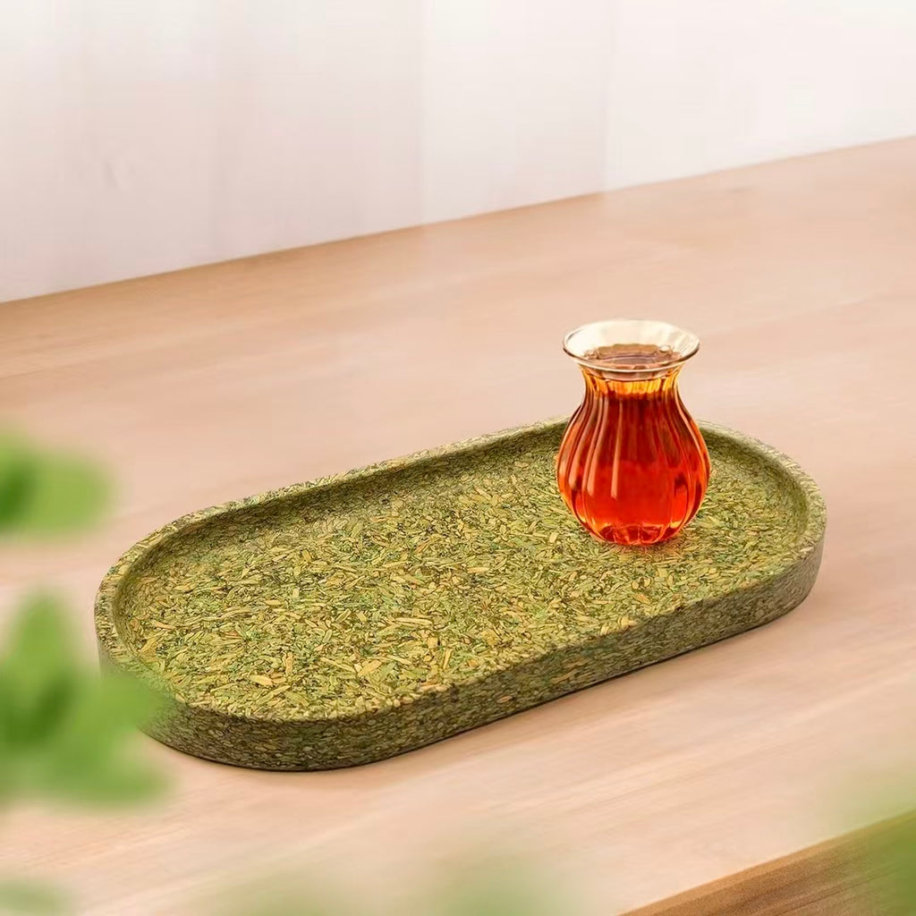 A biodegradable green oval tea tray with a glass cup of black tea, heat-resistant and moisture-proof lifestyle display.
