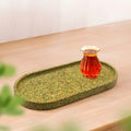 A biodegradable green oval tea tray with a glass cup of black tea, heat-resistant and moisture-proof lifestyle display.
