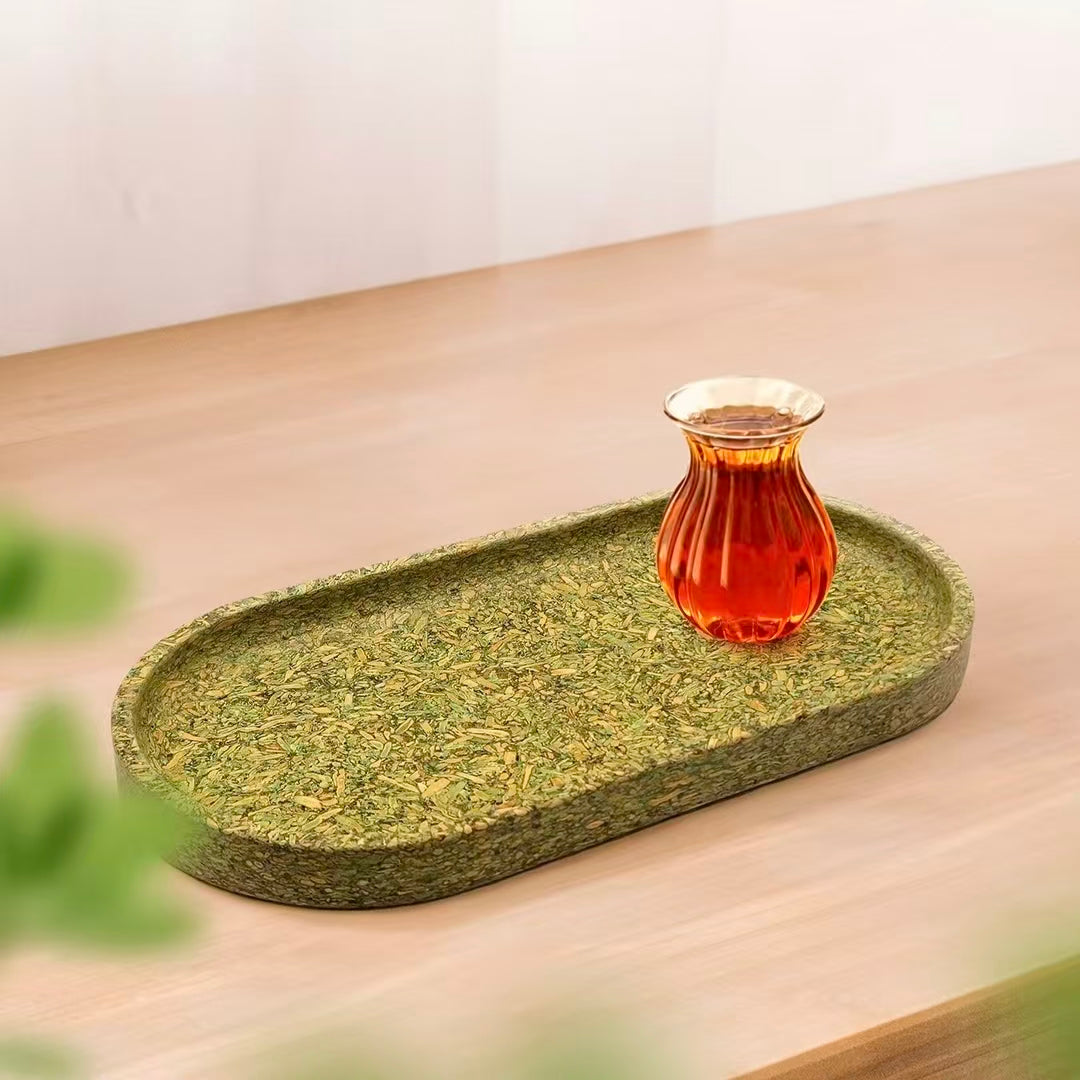 A biodegradable green oval tea tray with a glass cup of black tea, heat-resistant and moisture-proof lifestyle display.
