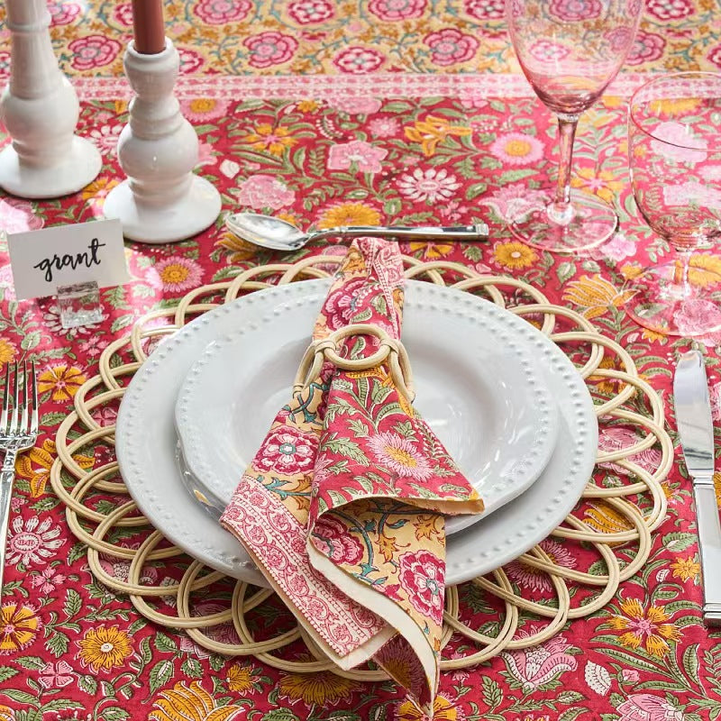 A bohemian style table setting featuring a white ceramic plate and floral napkin arranged on top of the woven rattan placemat.