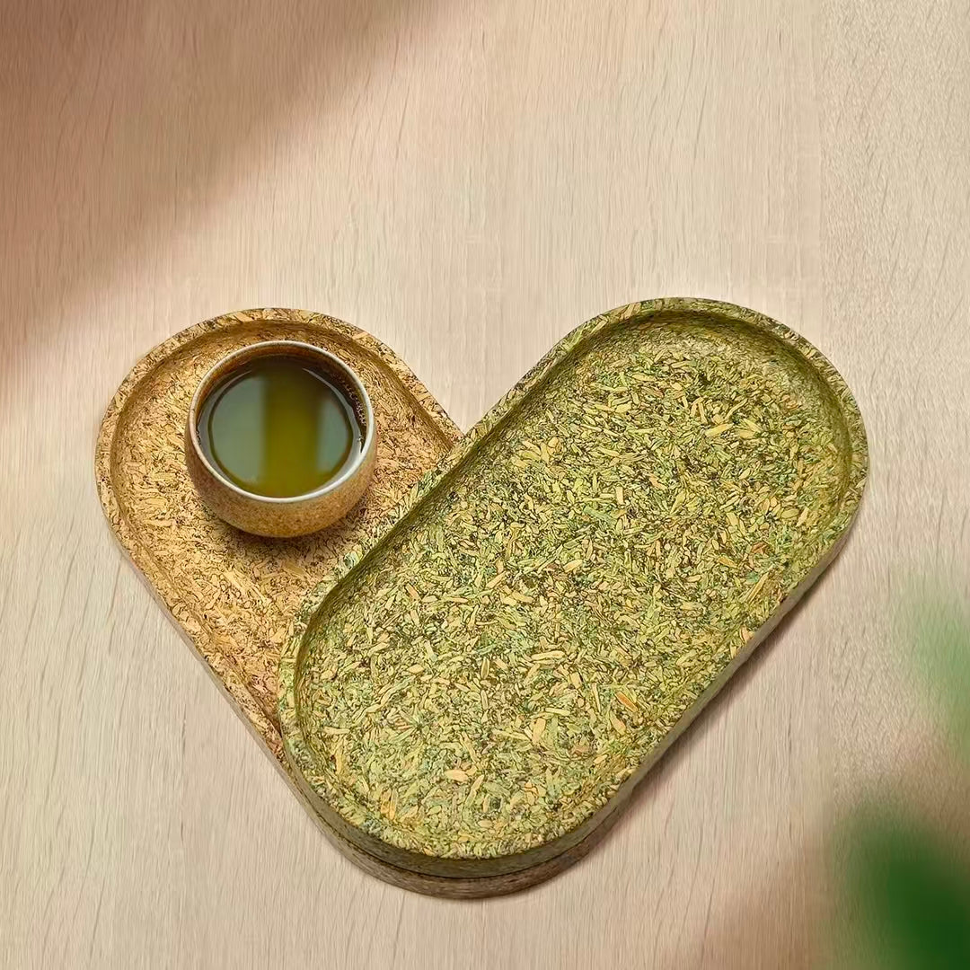Two oval tea dregs composite trays arranged in a heart shape on a wooden surface with a matching mini tea cup.
