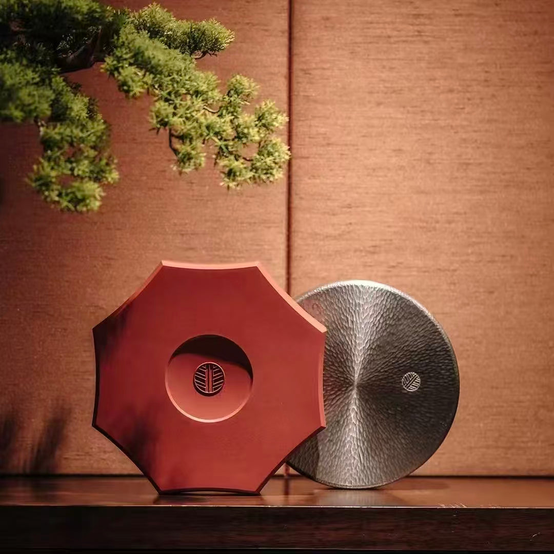  An elegant display of premium eco-friendly gift boxes on a dark wooden shelf, featuring an imperial red octagonal curved box and a silver hammered-texture round tin, complemented by a bonsai pine tree.