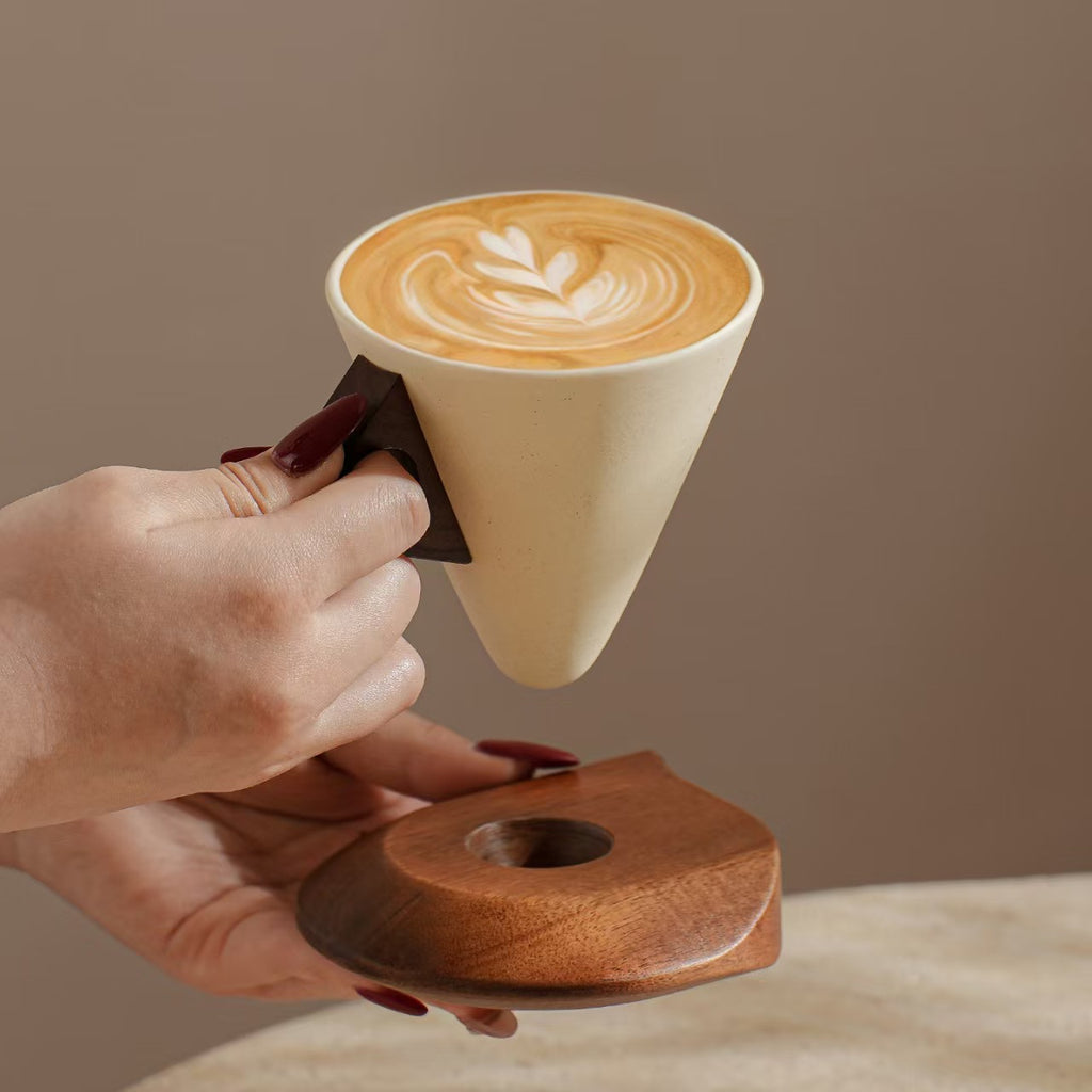 Close-up of hand holding geometric cone stoneware coffee mug with hollow wooden handle
