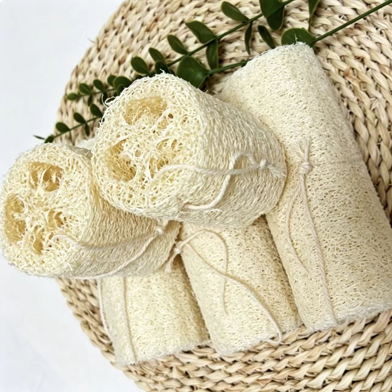 Stacked natural loofah dish scrubbers on rattan mat, sustainable kitchen cleaning supplies
