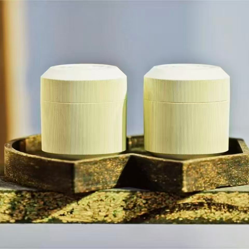 Two minimalist sage green ribbed tea canisters made from premium tea-fiber bio-composite material, displayed on an organic textured display riser.