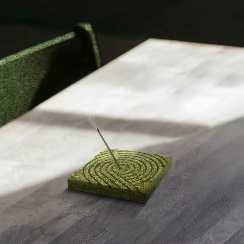 Lighted incense stick burning on a square green tea fiber pressed panel incense holder
