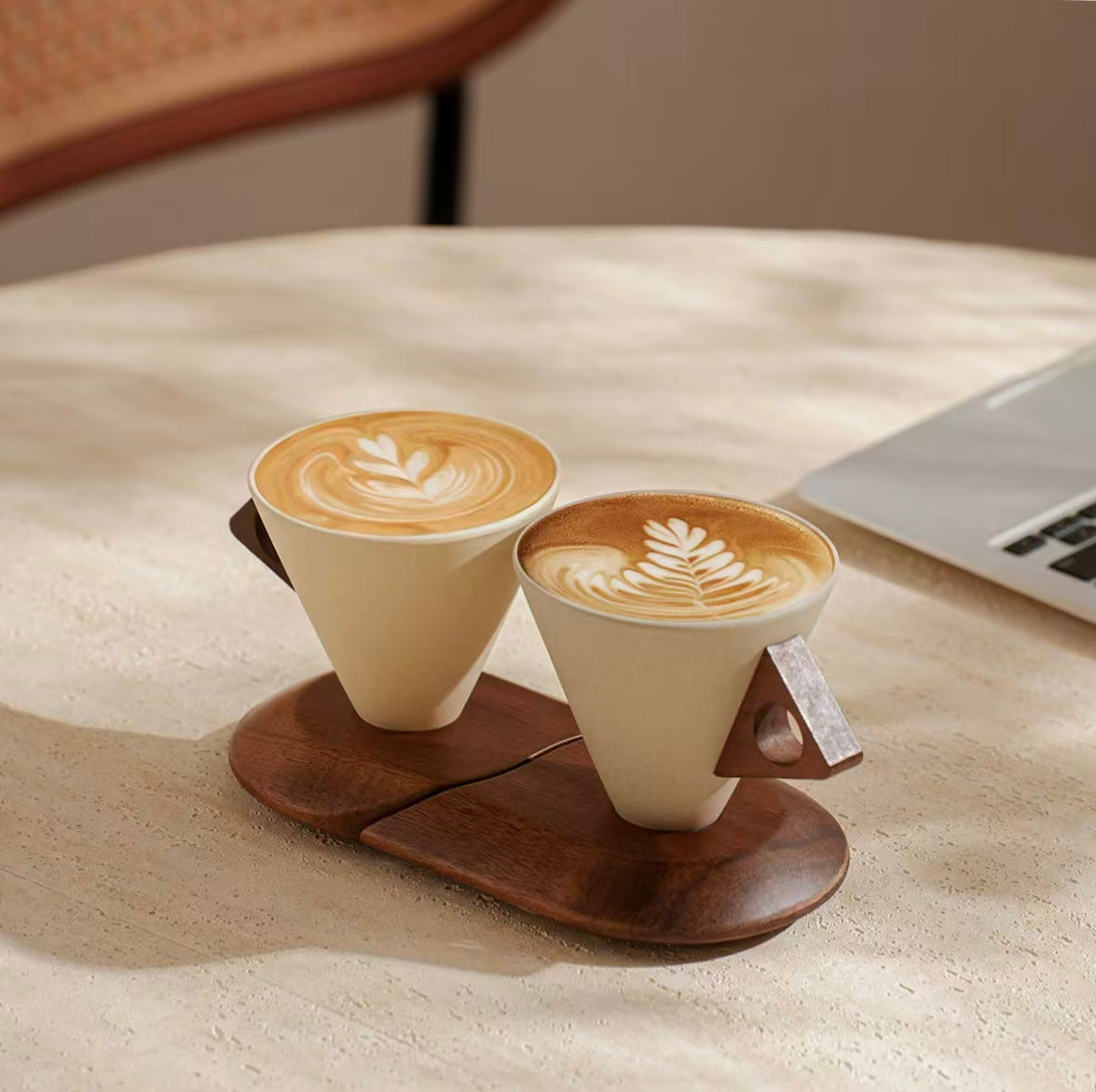 Pair of cone-shaped stoneware coffee mugs with latte art, wooden handle and stand on home office desk

