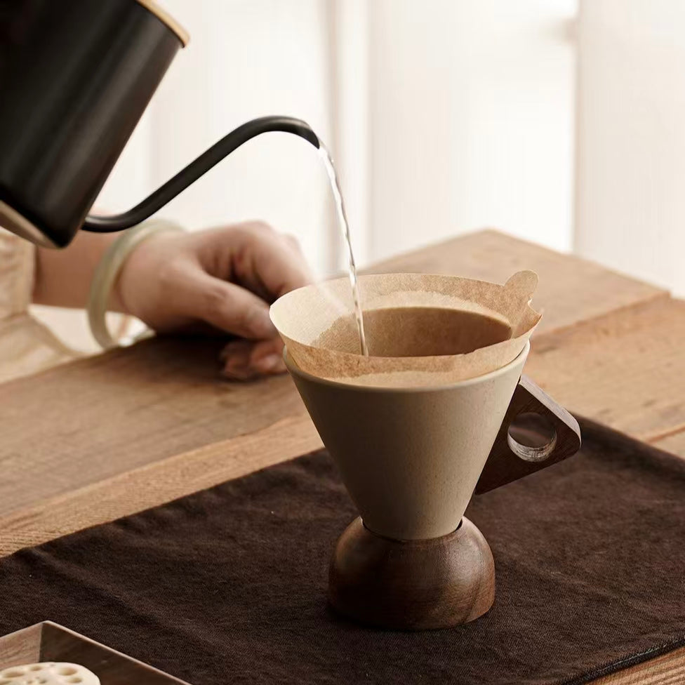 Wabi sabi conical ceramic coffee dripper with filter paper, wooden round base, home pour over coffee brewing scene, eco friendly kitchen table decor 