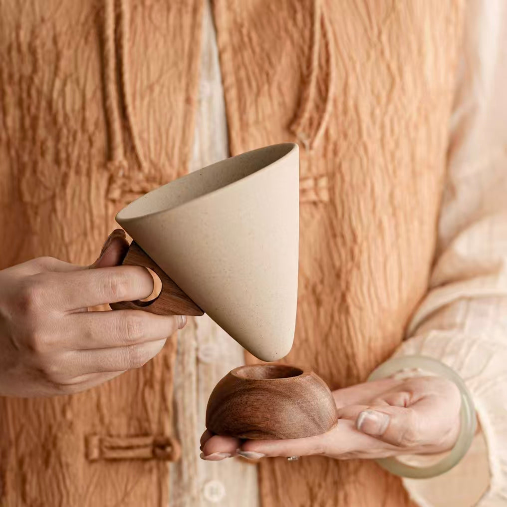 Handheld display of speckled ceramic coffee filter cup with cutout wooden handle, removable solid wood stand, minimalist sustainable coffee tableware 